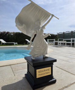 Sculpture de la statue de Ségurane par Florence Fabris : figure féminine blanche tenant un drapeau sur un socle noir avec plaque gravée SÉGURANE, exposée dans un intérieur chic avec vue sur Nice.