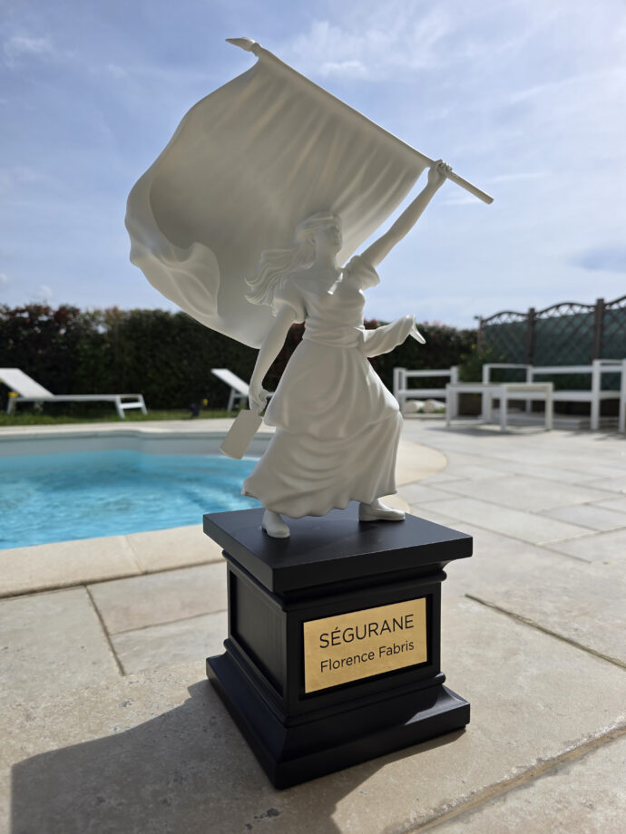 Sculpture de la statue de Ségurane par Florence Fabris : figure féminine blanche tenant un drapeau sur un socle noir avec plaque gravée SÉGURANE, exposée dans un intérieur chic avec vue sur Nice.