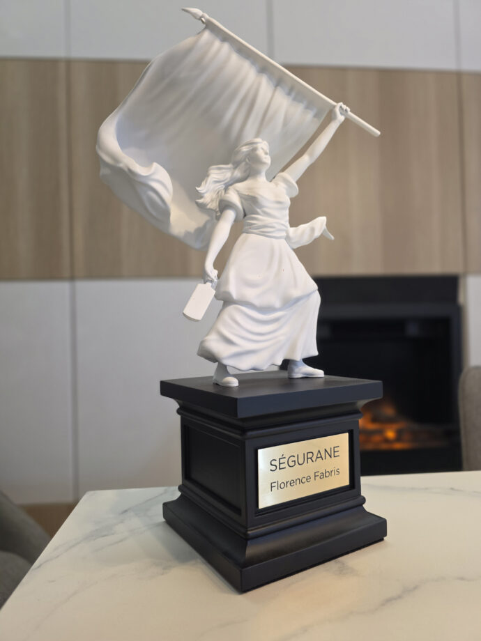 Sculpture de la statue de Ségurane par Florence Fabris : figure féminine blanche tenant un drapeau sur un socle noir avec plaque gravée SÉGURANE, exposée dans un intérieur chic avec vue sur Nice.
